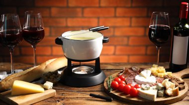 Kapalı masa üzerinde erimiş peynir, şarap ve atıştırmalıklarla fondü tenceresi (caquelon), yakın plan