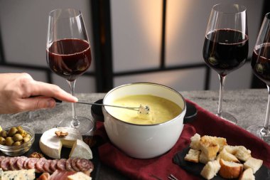 Bir kadın peyniri fondü kabına (caquelon) bandırıyor. Eritilmiş peyniri kapalı bir masada, yakın plan.