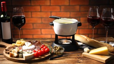 Kapalı masa üzerinde erimiş peynir, şarap ve atıştırmalıklarla fondü tenceresi (caquelon), yakın plan