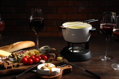 Kapalı masa üzerinde eritilmiş peynir, şarap ve atıştırmalıklar ile fondü tenceresi (caquelon)