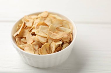 Beyaz ahşap masada kasede kurutulmuş sarımsak taneleri, yakın plan.