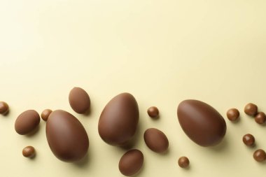 Paskalya kutlaması. Sarı arka planda bir sürü çikolata yumurtası ve sürükleyici var, düz bir zeminde metin için yer var.