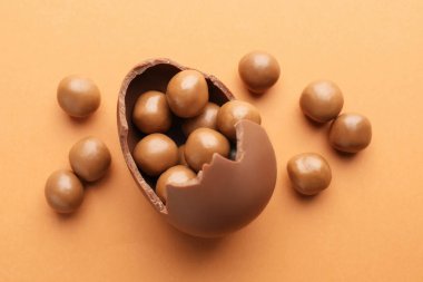 Çikolatalı Paskalya yumurtası soluk turuncu arka planda şekerli, düz yatıyordu.