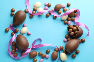 Çikolatalı Paskalya yumurtaları ve açık mavi arka planda menekşe kurdeleleri. Metin için boşluk