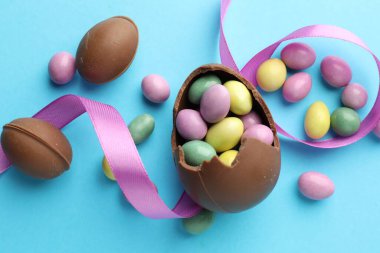 Çikolatalı Paskalya yumurtaları ve açık mavi arka planda menekşe kurdelesi.