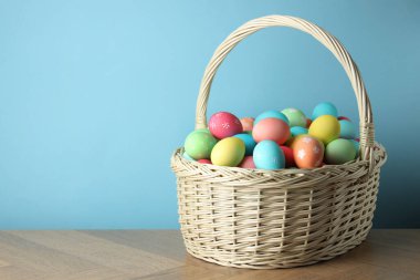 Güzel dekore edilmiş Paskalya yumurtaları hasır sepetin içinde ahşap masanın üzerinde açık mavi arka planda, metin için yer var.