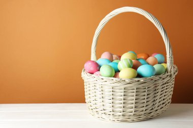 Güzel dekore edilmiş Paskalya yumurtaları hasır sepetin içinde beyaz ahşap masa üzerinde kahverengi arkaplan, metin için boşluk