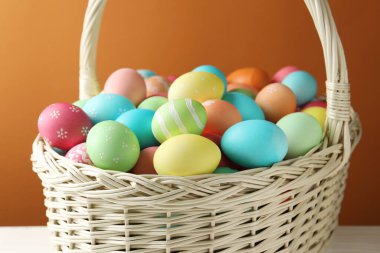 Hasır sepetteki güzel Paskalya yumurtaları kahverengi arka planda, yakın plan.