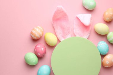 Mutlu Paskalyalar. Şirin tavşan kulakları, boyalı yumurtalar ve pembe arka planda boş podyum, düz yatış. Metin için boşluk