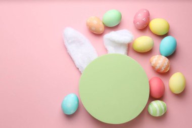 Mutlu Paskalyalar. Şirin tavşan kulakları, boyalı yumurtalar ve pembe arka planda boş podyum, düz yatış. Metin için boşluk