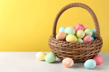 Beyaz masada sarı arka planda sepetteki güzel Paskalya yumurtaları. Metin için boşluk
