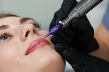 Güzellik uzmanı genç bir bayana kalıcı dudak makyajı yapıyor.