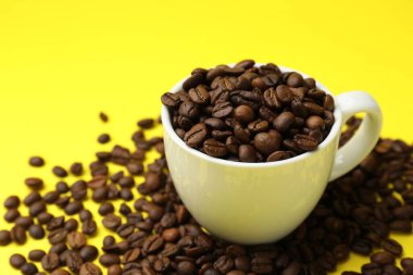 Aromatik kahve çekirdekleri ve fincanlar sarı arka planda, yakın plan.