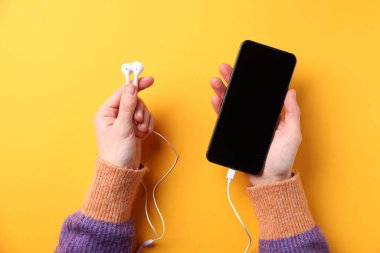 Sarı arka planda kulaklıklı akıllı telefonu olan bir kadın.