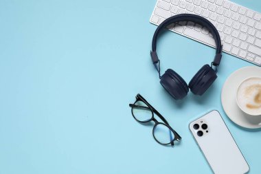 Kulaklıklar, akıllı telefon, bilgisayar klavyesi, açık mavi arka planda kahve ve bardaklar, düz yatak. Metin için boşluk