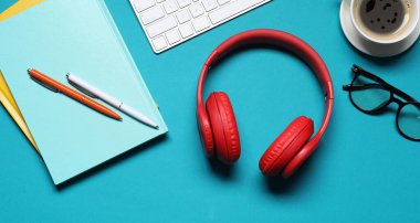 Açık mavi arkaplan üzerinde kulaklık ve kırtasiye ile düz kompozisyon yatıyordu