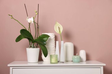 Koyu bej duvarın yanındaki dolapta çiçek dekoru ve yanan mum olan farklı güzel vazolar.