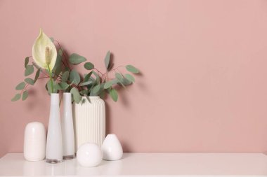 Bej duvarın yanındaki dolapta çiçek dekoru olan farklı güzel vazolar.