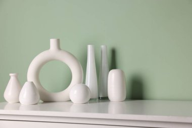 Soluk yeşil duvarın yanındaki dolapta güzel vazolar var.