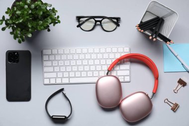 Kulaklıklar, bilgisayar klavyesi, akıllı saat, akıllı telefon, kırtasiye, gözlük ve çiçek dekoru açık gri arka planda, düz konum