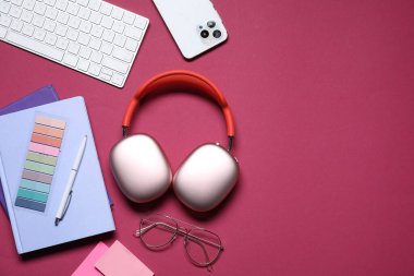 Kulaklık, akıllı telefon, bilgisayar klavyesi, kırtasiye malzemesi ve kırmızı arka planda gözlük, düz konum. Metin için boşluk