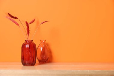Turuncu duvarın yanındaki ahşap masada çivili güzel vazolar var.