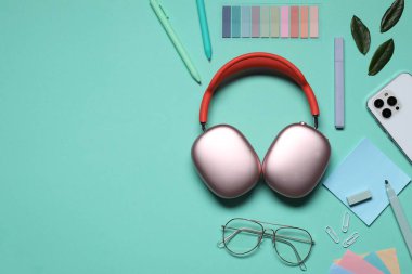 Kulaklık, akıllı telefon, gözlük, kırtasiye malzemesi ve turkuaz arka planda yeşil yapraklar. Metin için boşluk
