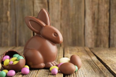 Mutlu Paskalyalar. Çikolatalı tavşan ve renkli şekerli yumurtalar ahşap masada, yakın plan. Metin için boşluk