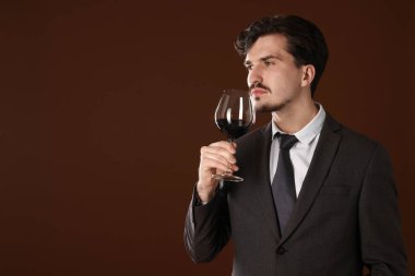 Profesyonel şarap garsonu kahverengi arka planda kırmızı şarap tadıyor. Metin için boşluk