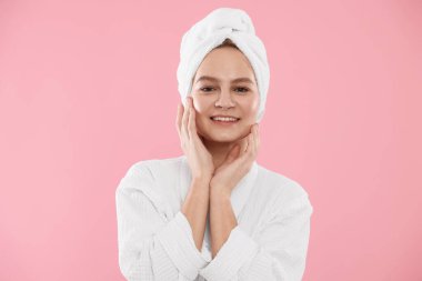 Pembe arka planda havluya sarılı güzel bir kadın.