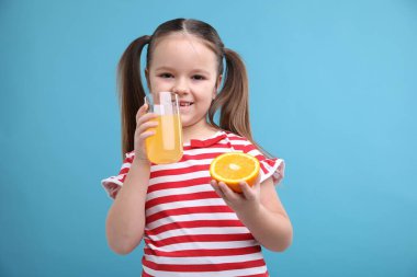 Bardakta portakal suyu ve açık mavi arka planda yarım meyve suyu olan küçük bir kız.