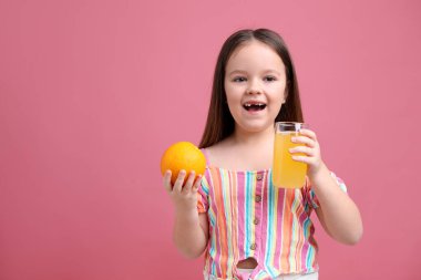 Bardakta portakal suyu ve pembe arka planda taze meyve olan küçük kız, mesaj için yer var.