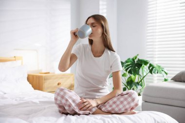 Evdeki yatakta bir fincan aromatik kahveyle güzel bir kadın.