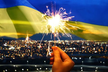 Ukrayna bayrağı ve şehir manzarasına karşı yanan maytaplar tutan bir kadın. Ulusal bayram tebrik kartı veya poster tasarımı