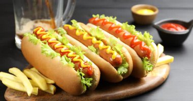 Bardağa soda doldurmak, ketçaplı lezzetli sosisliler, hardal, marul ve patates kızartmalarını siyah masaya koymak.