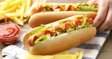 Ahşap masada soslu ve marullu lezzetli sosisli sandviç yiyen bir kadın.