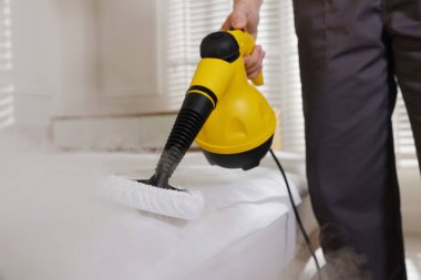 Haşere kontrol işçisi yatağı temizliyor, kapalı alanda buhar temizleyicisiyle, yakın plan