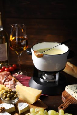 Erimiş peynir, şarap ve ahşap masada atıştırmalıklarla fondü tenceresi (caquelon)