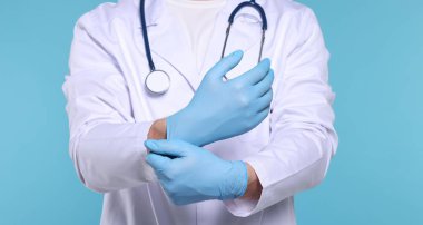 Doktor açık mavi arka plana eldiven takıyor, yakın plan.