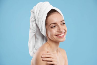 Saçları açık mavi arka planda havluya sarılı güzel bir kadın.