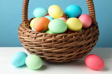 Güzel dekore edilmiş Paskalya yumurtaları hasır sepetin içinde beyaz ahşap masanın üzerinde açık mavi arka planda, yakın plan