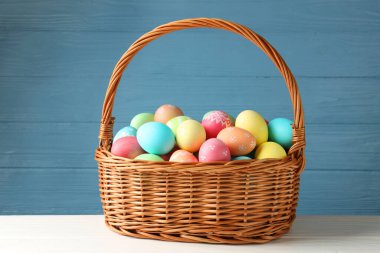 Güzel dekore edilmiş Paskalya yumurtaları hasır sepetin içinde beyaz ahşap masada.