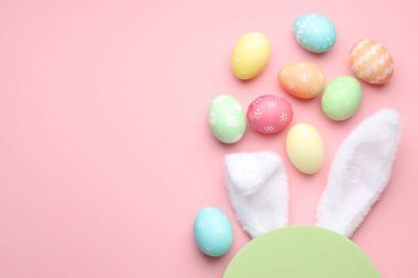Mutlu Paskalyalar. Şirin tavşan kulakları, boyalı yumurtalar ve pembe arka planda boş podyum, düz yatış. Metin için boşluk