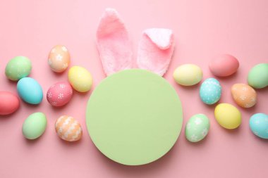 Mutlu Paskalyalar. Şirin tavşan kulakları, boyalı yumurtalar ve pembe arka planda boş podyum, düz yatış. Metin için boşluk