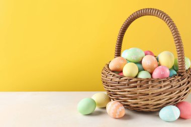 Beyaz masada sarı arka planda sepetteki güzel Paskalya yumurtaları. Metin için boşluk