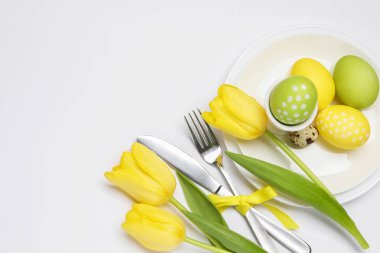 Paskalya kutlaması. Lale çiçekli şenlik masası, beyaz arka planda boyanmış bıldırcın yumurtaları, düz yatış. Metin için boşluk