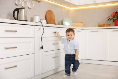 Evde çocuk güvenliği. Küçük çocuk mutfakta elektrikli su ısıtıcısına uzanıyor.