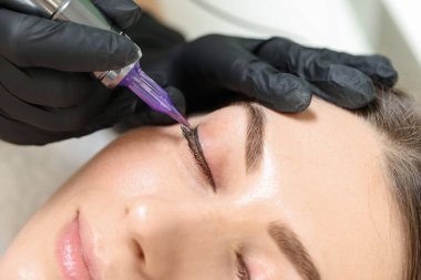 Güzellik uzmanı genç bir kadına kalıcı göz kalemi makyajı yapıyor.