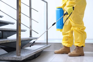 Koruyucu kıyafetli bir haşereci merdivenlere böcek ilacı sıkıyor, yakın plan. Metin için boşluk