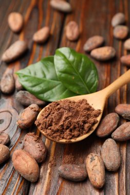 Doğal kakao çekirdekleri, toz ve yeşil yapraklar ahşap masada, yakın plan.